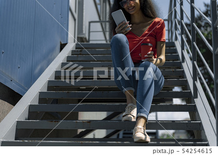 Attractive young woman in glasses sitting on stairs and using cellphone 54254615