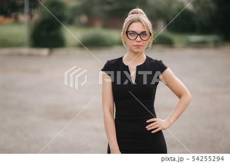 Young attractive female techer in black dress with sunglasses standing outside. Background of school Young attractive female techer in black dress with sunglasses standing outside. Background of school 54255294
