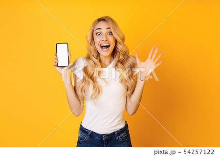 Amazed Girl Showing Blank Smartphone Screen, Yellow Background Amazed Girl Showing Blank Smartphone Screen, Yellow Background 54257122