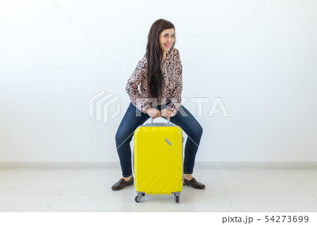 Young woman posing sitting on a yellow suitcase against the background of a white wall with copy Young woman posing sitting on a yellow suitcase against the background of a white wall with copy 54273699