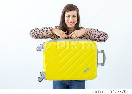 Joyful smiling young brunette woman posing with a yellow suitcase while waiting for a vacation. The Joyful smiling young brunette woman posing with a yellow suitcase while waiting for a vacation. The 54273702