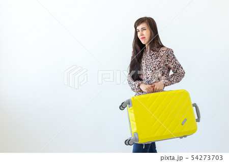 Joyful smiling young brunette woman posing with a yellow suitcase while waiting for a vacation. The 54273703
