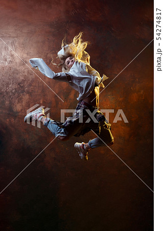 Photo of jumping blonde dancer woman looking back in torn jeans and sneakers on dark brown Photo of jumping blonde dancer woman looking back in torn jeans and sneakers on dark brown 54274817