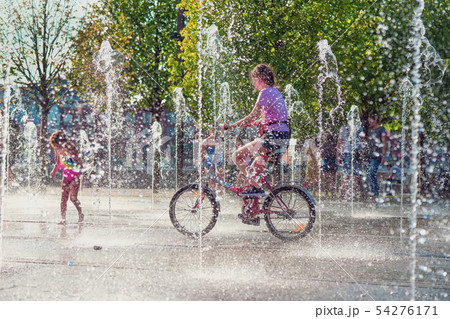 Summer, heat, a girl riding a bike among fountains, people cool in jets of water 54276171