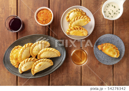 Empanadas with sauces and wine, shot from the top on a dark rustic wooden background 54276342