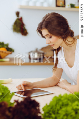Young woman looking for a new recipe for cooking in a kitchen. Housewife is making online shopping Young woman looking for a new recipe for cooking in a kitchen. Housewife is making online shopping 54276659