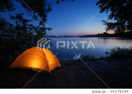 Illuminated from inside orange tent and surfboard on beach 54279194