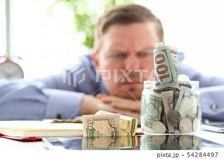 Man looking at jar full of money thinking about his debts Man looking at jar full of money thinking about his debts 54284497