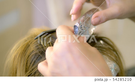 close-up. Hair dyeing at the hairdresser. hands of a barber dye hair strands and wrap in foil 54285210
