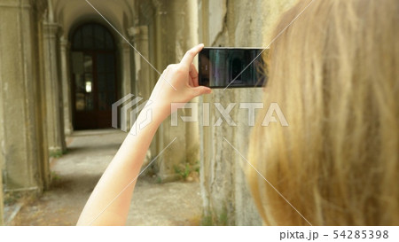 Young woman taking pictures with phone of a colonnade of an old castle 54285398