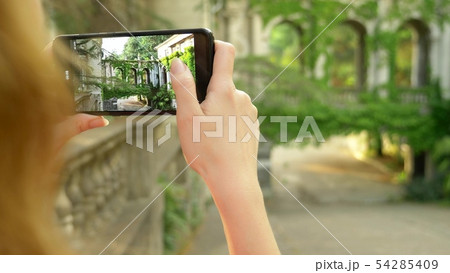 Young woman taking pictures with phone of a colonnade of an old castle 54285409