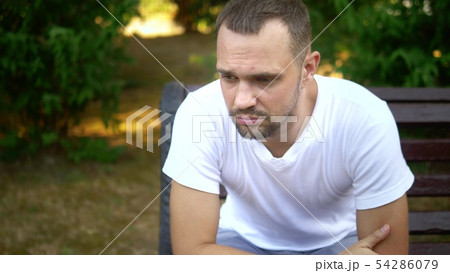 Depressed Sad young man sitting alone on a bench in a summer park. copy space 54286079