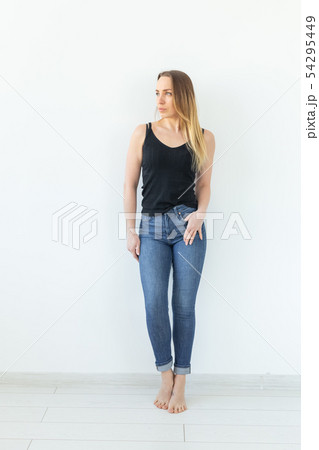 Style and people concept - young woman in jeans standing over the white wall and looks like sexy 54295449
