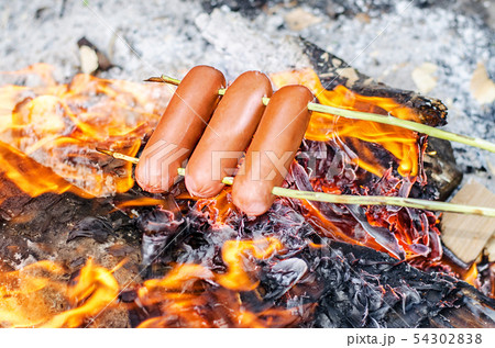 Grilling sausages over an open fire outdoors. 54302838