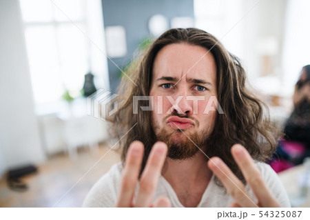 A portrait of young man with long hair indoors, fingers forming V for victory. 54325087
