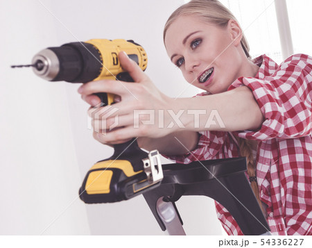 Woman using drill on ladder 54336227
