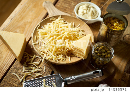 Shredded yellow cheese with cheese grater and capers and basil on kitchen table 54336571