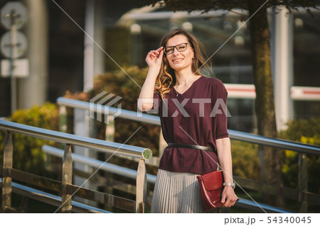 Caucasian adult lady woman in glasses posing near office building outside. Business lady in skirt 54340045