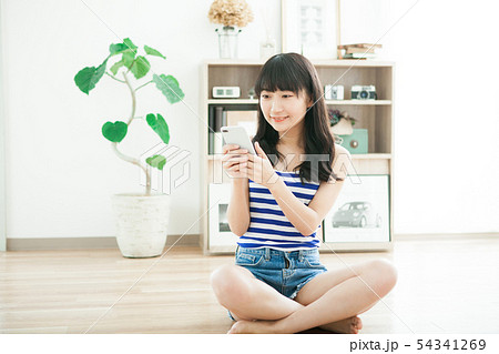 部屋でスマホを使う夏服の女の子の写真素材
