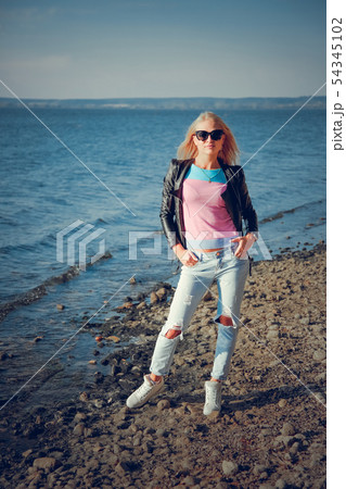 Beautiful blonde in ripped jeans posing on the shore of the blue sea 54345102