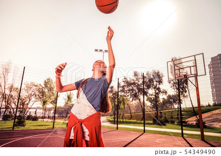 Flexible young lady in comfortable outfit showing tricks with basketball ball Flexible young lady in comfortable outfit showing tricks with basketball ball 54349490
