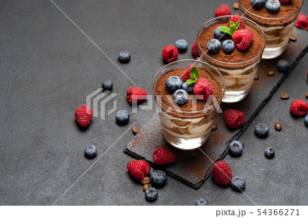 Classic tiramisu dessert with blueberries and raspberries in a glass on stone serving board on dark Classic tiramisu dessert with blueberries and raspberries in a glass on stone serving board on dark 54366271