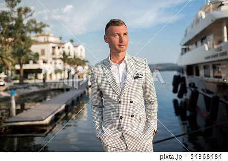 Handsome businessman is wearing white fashion costume stands on the background of the bay with Handsome businessman is wearing white fashion costume stands on the background of the bay with 54368484