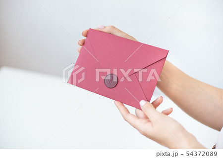 Close-up photo of female hands holding a silver invitation envelope with a wax seal, a gift Close-up photo of female hands holding a silver invitation envelope with a wax seal, a gift 54372089