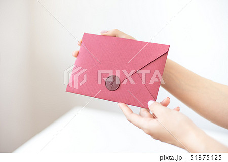 Close-up photo of female hands holding a silver invitation envelope with a wax seal, a gift 54375425