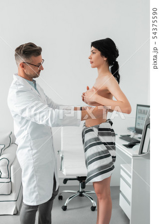 Dark-haired woman with naked breast visiting plastic surgeon Dark-haired woman with naked breast visiting plastic surgeon 54375590