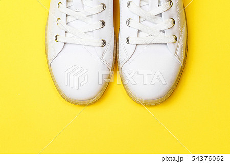 White sneakers are lying on a pastel yellow background. White sneakers are lying on a pastel yellow background. 54376062