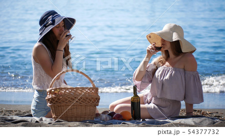 Two young women sitting near the sea and having a picnic - drinking wine Two young women sitting near the sea and having a picnic - drinking wine 54377732