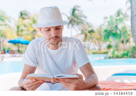 Caucasian guy relaxing near pool with amazing view and reading book 54384459