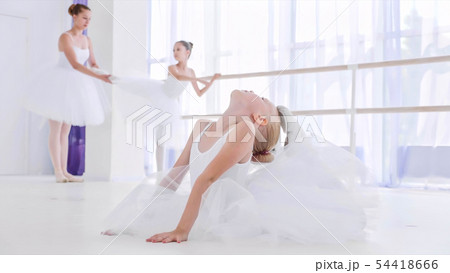 Child girl ballerina in white tutu is doing stretch exercises on ballet lesson. 54418666