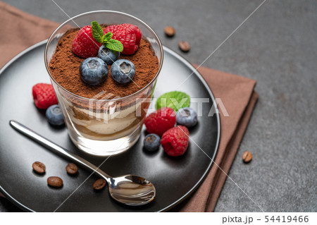 Classic tiramisu dessert with blueberries and raspberries in a glass on dark concrete background 54419466