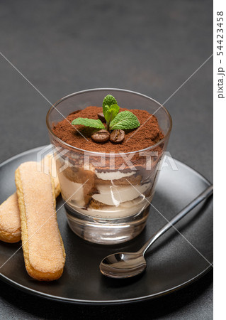 Classic tiramisu dessert in a glass and savoiardi cookies on dark concrete background 54423458