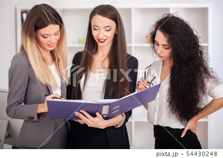 Team portrait of happy businesswomen standing on office corridor, looking at camera, smiling. 54430248