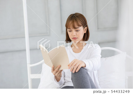 Asian woman sitting on bed in bedroom reading book 54433249