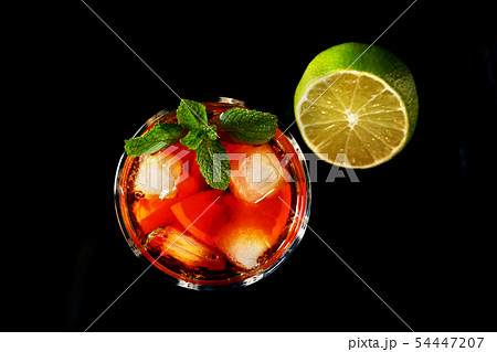 Glass of Dark Rum Cocktail with lime, orange, ice cubes and mint leaves on black mirror background 54447207