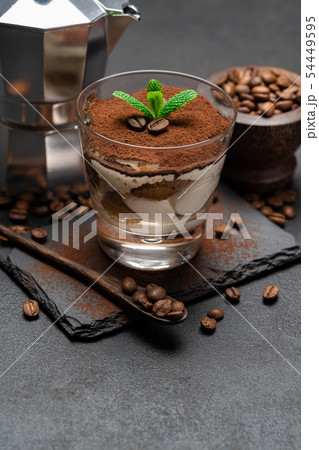 Classic tiramisu dessert in a glass and coffee maker on stone serving board on dark concrete Classic tiramisu dessert in a glass and coffee maker on stone serving board on dark concrete 54449595