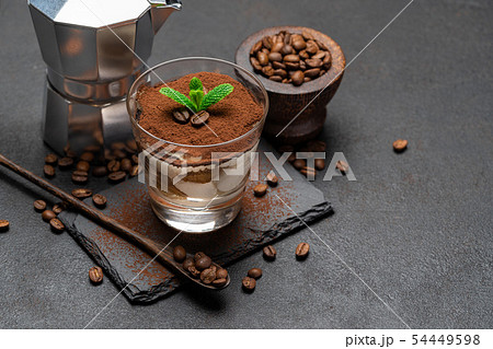 Classic tiramisu dessert in a glass and coffee maker on stone serving board on dark concrete Classic tiramisu dessert in a glass and coffee maker on stone serving board on dark concrete 54449598