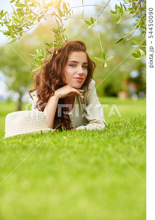 Beautiful smiling woman lying on a grass outdoor. 54450090