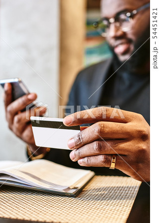 Close up shot of African man's hands holding mobile and credit card Close up shot of African man's hands holding mobile and credit card 54451421