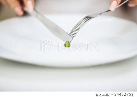 Eating disorder. Girl is holding a plate and trying to put a pea on the fork Eating disorder. Girl is holding a plate and trying to put a pea on the fork 54452758