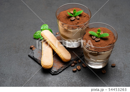 Classic tiramisu dessert in a glass and savoiardi cookies on dark concrete background Classic tiramisu dessert in a glass and savoiardi cookies on dark concrete background 54453263
