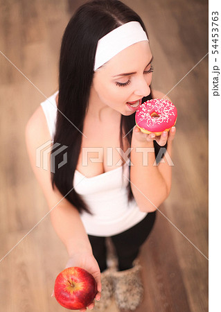 Beautiful young woman making choice between apple and donut, close up 54453763