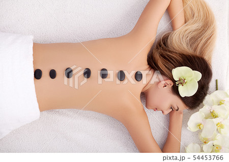 Spa. Young woman doing hot stone therapy. Professional beautician massaging female back by stones Spa. Young woman doing hot stone therapy. Professional beautician massaging female back by stones 54453766