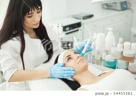 Doctor with Ultrasonic scraber. Doing procedure of ultrasonic cleaning of face. Model, profile Doctor with Ultrasonic scraber. Doing procedure of ultrasonic cleaning of face. Model, profile 54455561