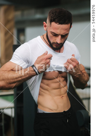 Young athlete posing with a torso for photography in gym. Bodybuilder, athlete with pumped muscles Young athlete posing with a torso for photography in gym. Bodybuilder, athlete with pumped muscles 54459976