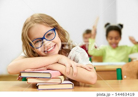 Child posing while sitting at desk and lying on books 54463419